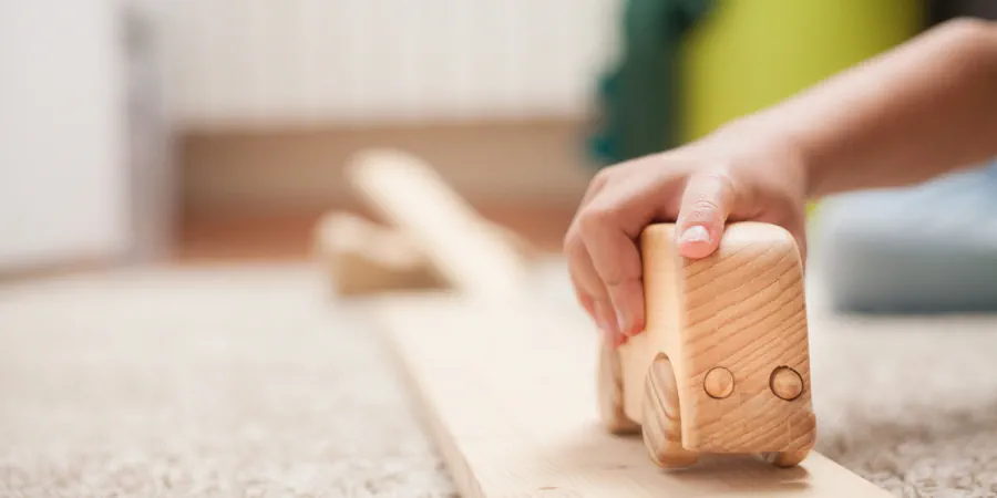 Mão de criança brincando com carrinho de madeira