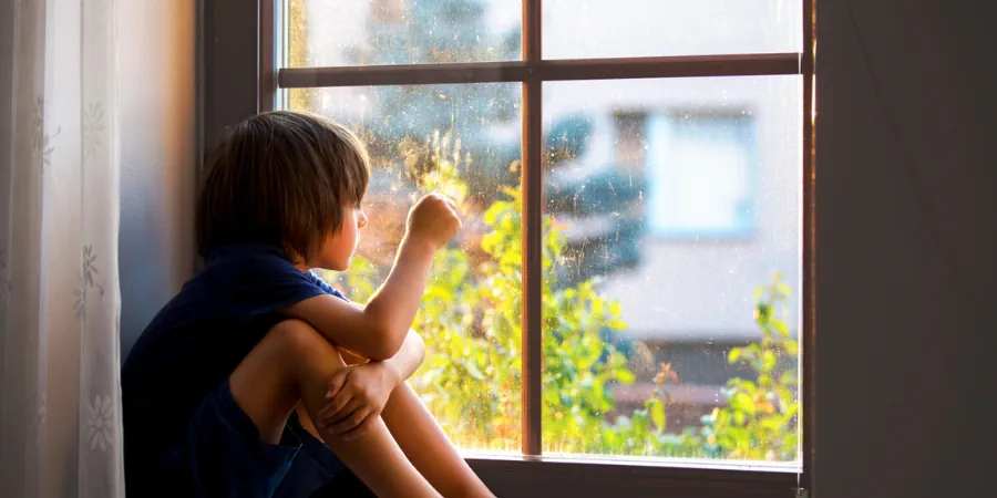 Criança sentada na janela olhando para fora, em momento de contemplação